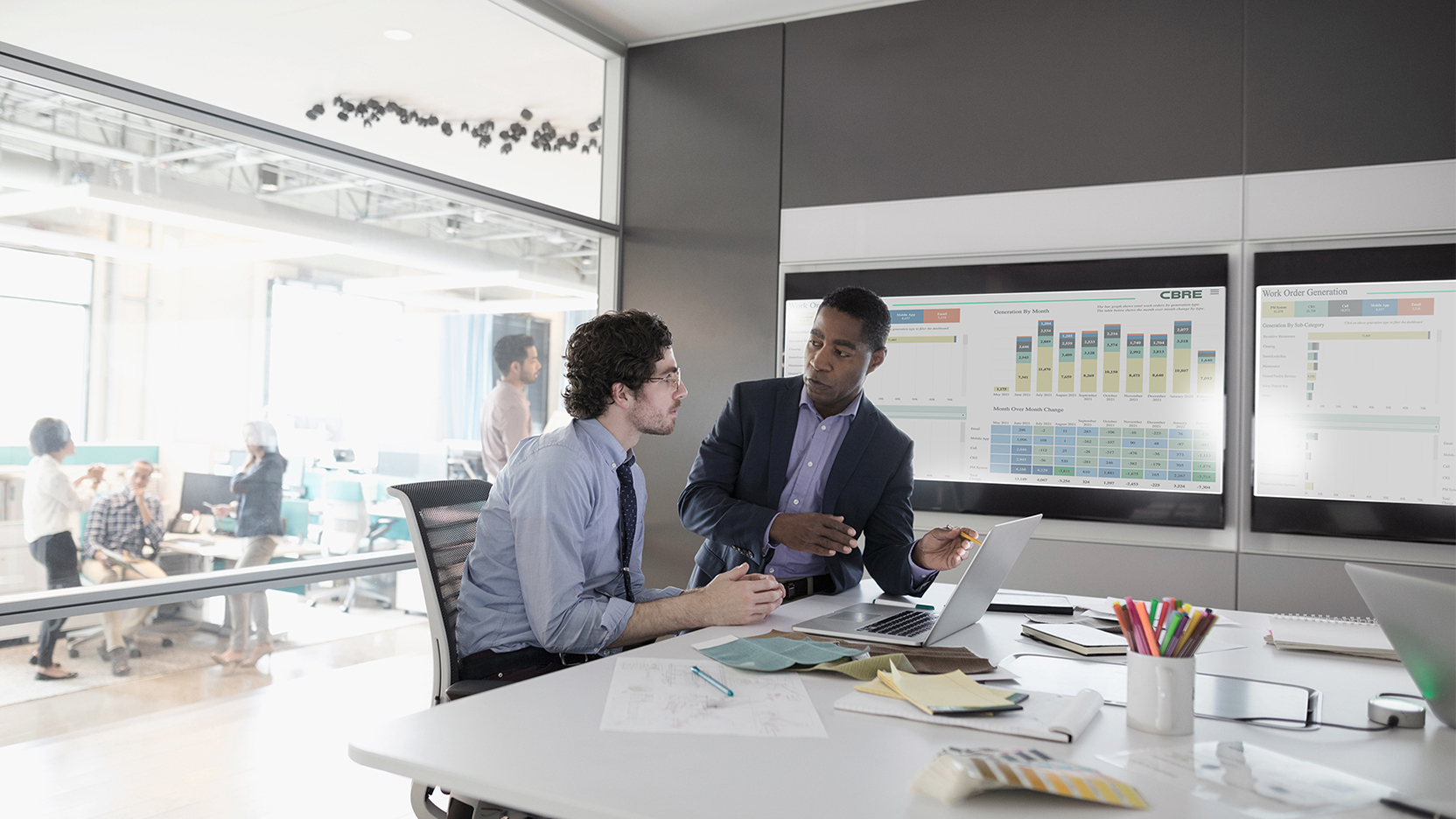 Male colleagues in discussion in open office with data projected on screens