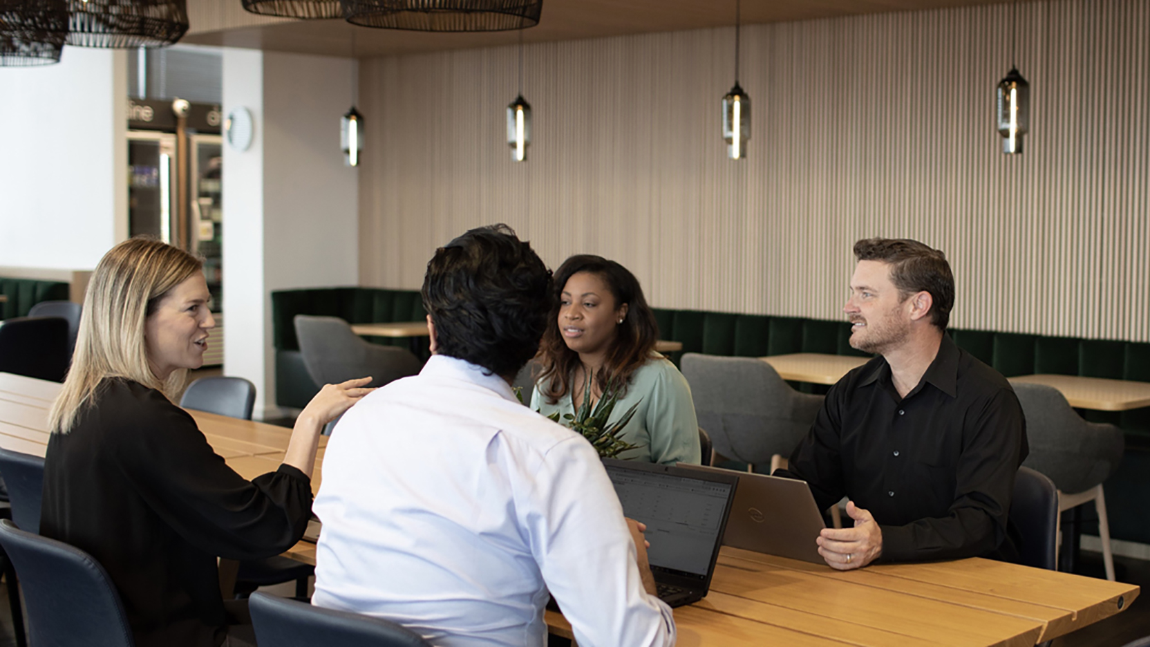 Colleagues gathered with laptops at a table in a common office space